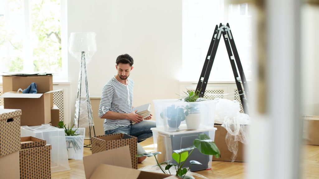 Man unpacking stuff from carton boxes after relocation to new ho