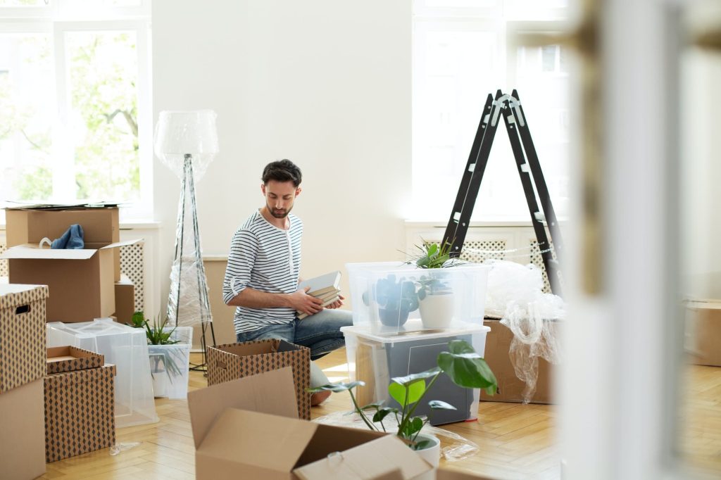 Man unpacking stuff from carton boxes after relocation to new ho