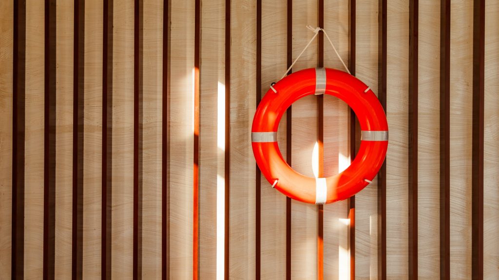 Red lifebuoy hanging on blue wooden wall of a port building