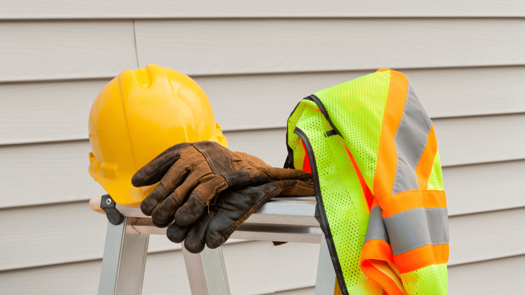 Casque de chantier jaune, gants de protection marron et gilet jaune, posés sur un tréteau - Ruff